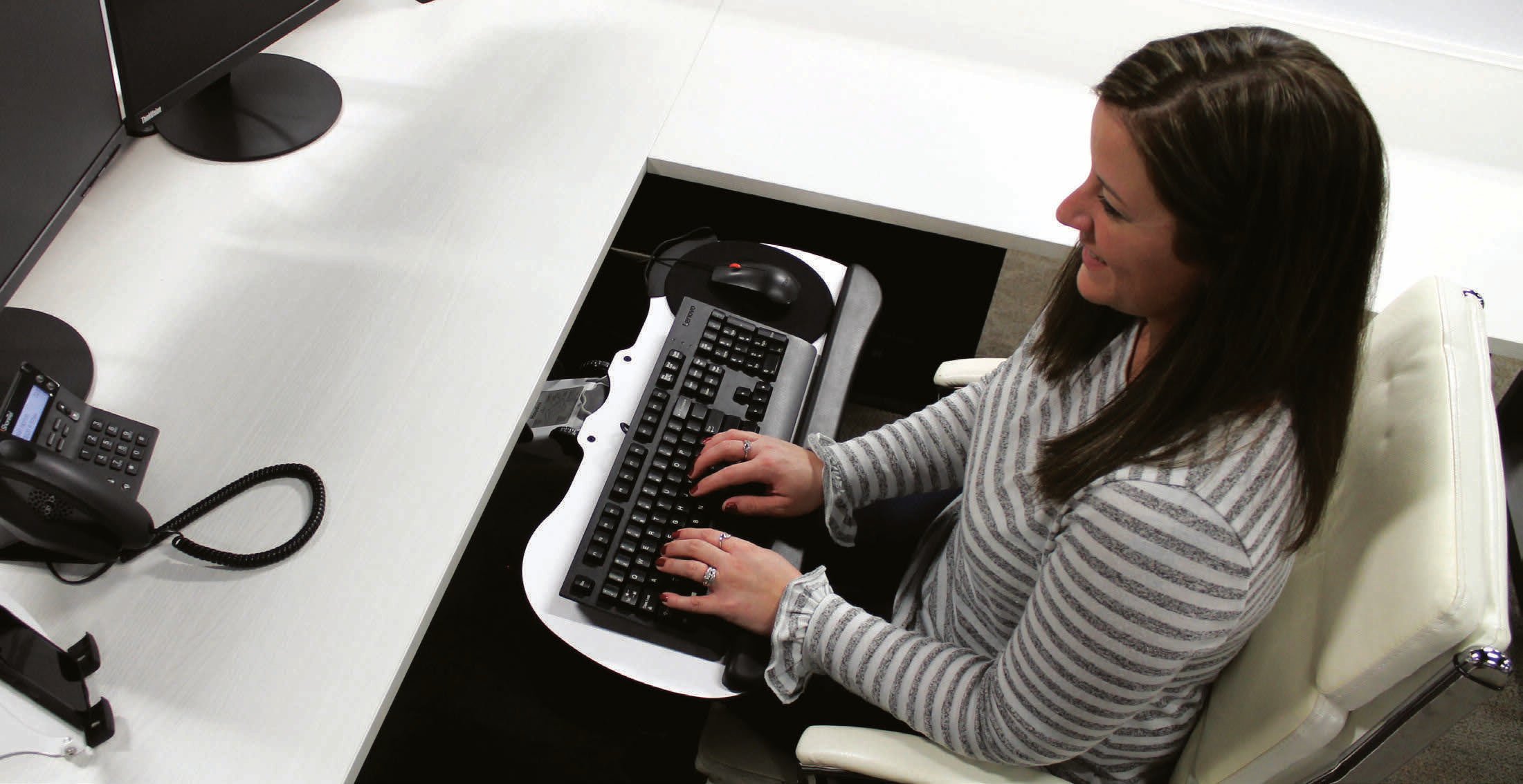 Woman working at a desk using an ergonomic computer keyboard tray 