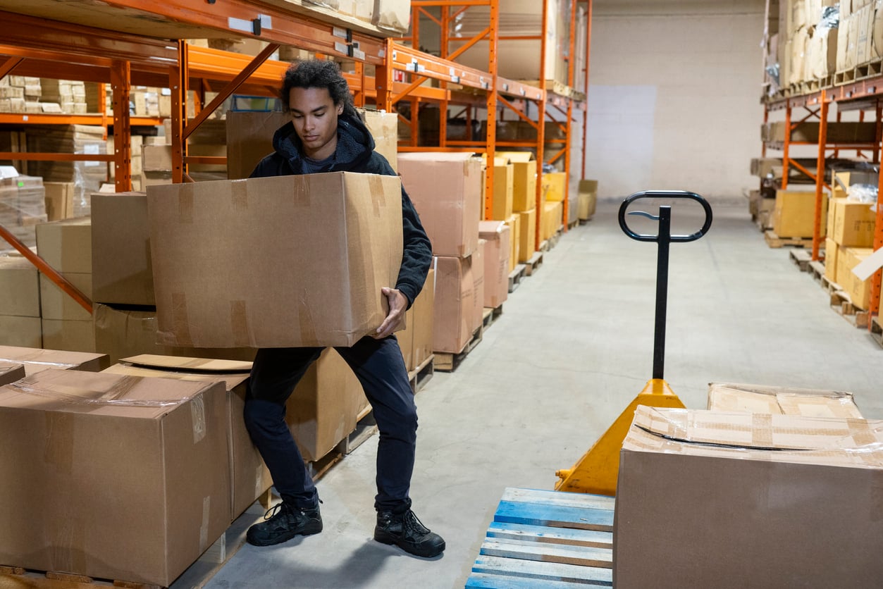 Worker lifting a box in a warehouse, showing ergonomically safe movement during real work