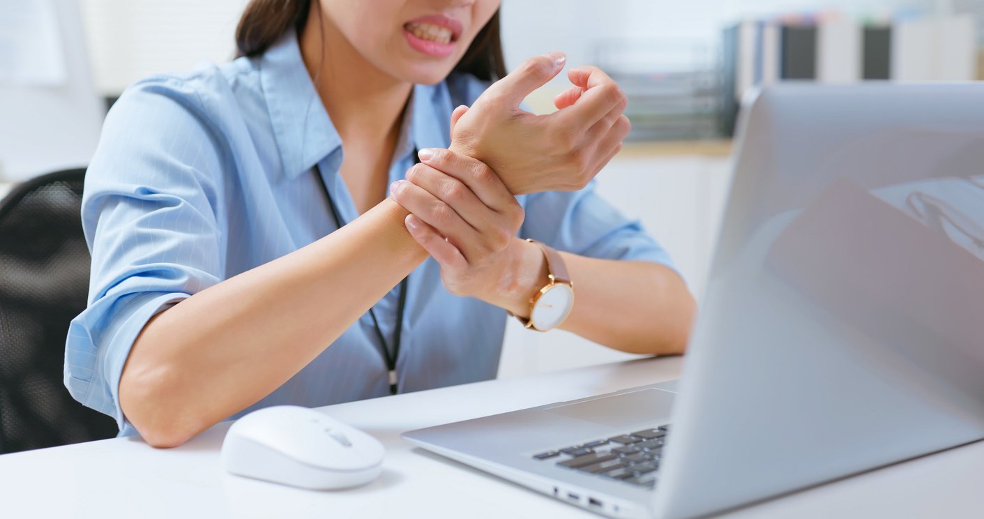 Employee experiencing wrist strain at computer workstation illustrating ergonomic injuries impact
